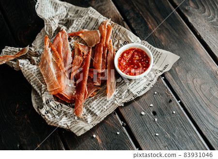 Dried chicken, dried poultry, cut into strips on parchment and wooden background. Served with ajiga or ketchup Dried chicken, dried poultry, cut into strips on parchment and wooden background. Served with ajiga or ketchup 83931046