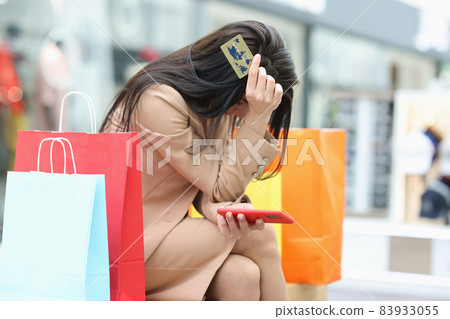Young woman sits in a mall with a credit card in her hands Young woman sits in a mall with a credit card in her hands 83933055