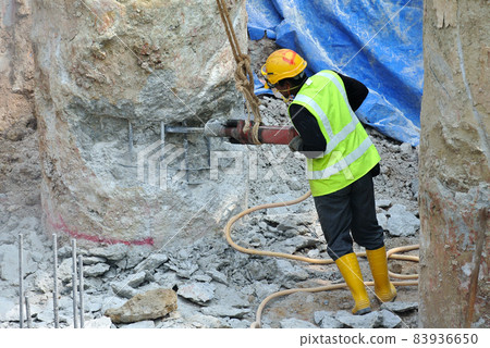 JOHOR, MALAYSIA -JANUARY 13, 2015: A construction workers cutting foundation pile using hacking method at the construction site. He using the heavy duty mobile hacker machine. JOHOR, MALAYSIA -JANUARY 13, 2015: A construction workers cutting foundation pile using hacking method at the construction site. He using the heavy duty mobile hacker machine. 83936650