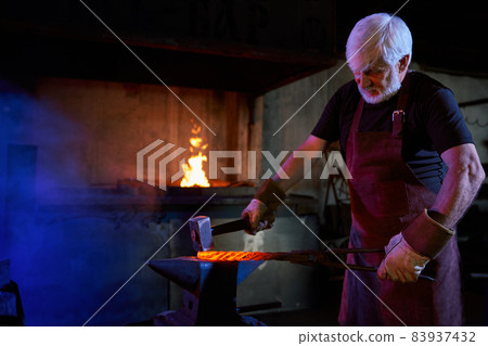 Aged blacksmith forged iron on anvil using heavy hammer 83937432