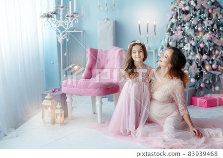 Mom and daughter in pink dresses near the Christmas tree in the apartment Mom and daughter in pink dresses near the Christmas tree in the apartment 83939468