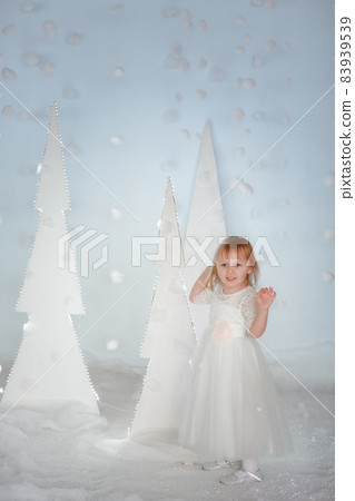 Cute girl in white Princess costume between white artificial glowing Christmas trees Cute girl in white Princess costume between white artificial glowing Christmas trees 83939539