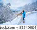 A man in warm clothes stands with a dog along a snowy mountain road 83940604