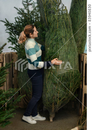 A woman choses a christmas trees wrapped in a net 83940830