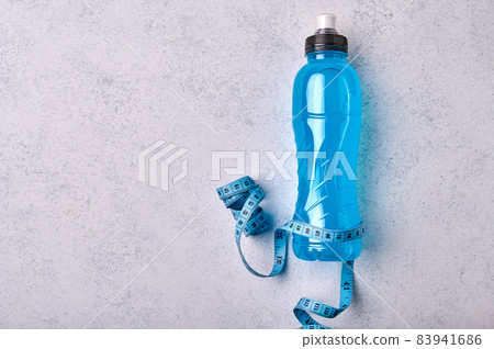Isotonic energy blue transparent sport drink in plastic bottle and measure tape on grey textured 83941686