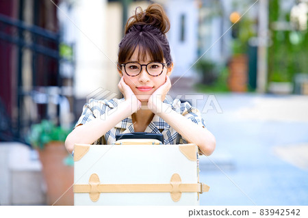 A smiling young woman taking a break while leaning on a travel bag 83942542