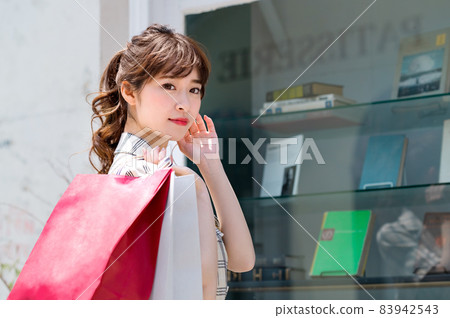 A young woman shopping with a paper bag in front of a shop window A young woman shopping with a paper bag in front of a shop window 83942543