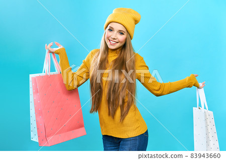 A young woman enjoying her shopping during a big Black Friday sale. Woman with shopping bags. Smiling girl in a yellow hat and yellow sweater on a blue background. A young woman enjoying her shopping during a big Black Friday sale. Woman with shopping bags. Smiling girl in a yellow hat and yellow sweater on a blue background. 83943660