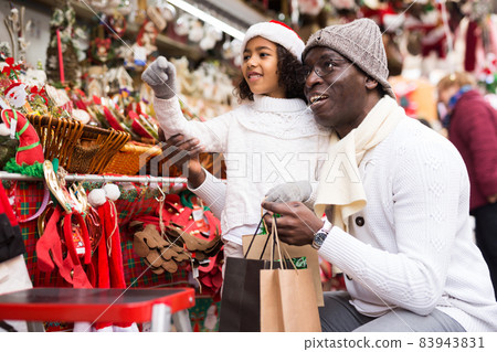 Girl with father choosing decorations and pointing to toys Girl with father choosing decorations and pointing to toys 83943831
