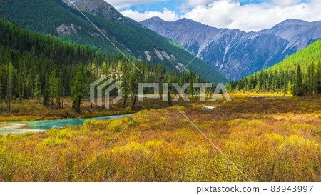 Swampy autumn plateau. Awesome highland scenery with beautiful glacial lake among sunlit hills and rocks against mountain range. 83943997
