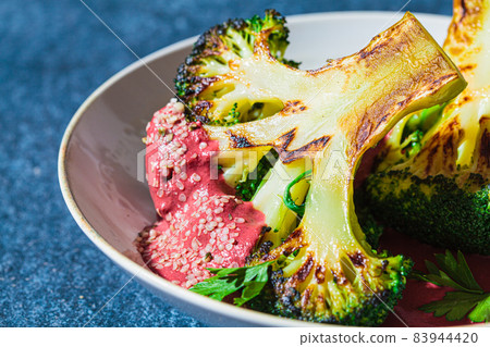 Grilled broccoli steak with pink beetroot sauce and hemp seeds in a white bowl, blue background. Healthy vegan food concept. 83944420