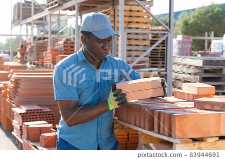 Construction shop worker stacks bricks on an open air site at summer day 83944691