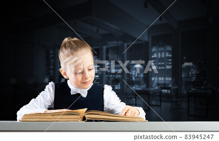 Smiling little girl sitting at desk with open book Smiling little girl sitting at desk with open book 83945247