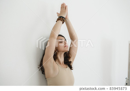 portrait of a young girl doing yoga sitting with her hands up against a white wall 83945873