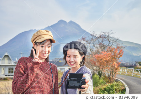 A young woman and a friend taking a commemorative photo with Mt. Yufu in the background on a girls' trip 83946099