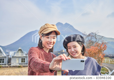 A young woman and a friend taking a commemorative photo with Mt. Yufu in the background on a girls' trip A young woman and a friend taking a commemorative photo with Mt. Yufu in the background on a girls' trip 83946100