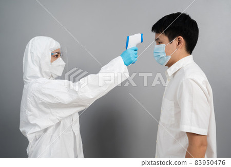 doctor in protective PPE suit using infrared thermometer measuring temperature with people 83950476