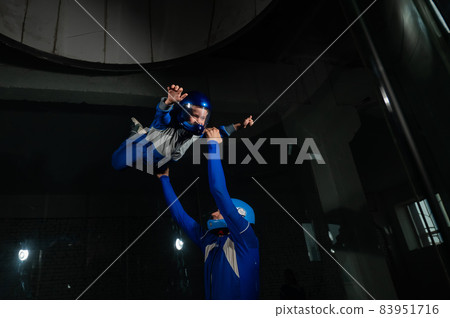 A man teaches a boy to fly in a wind tunnel. 83951716