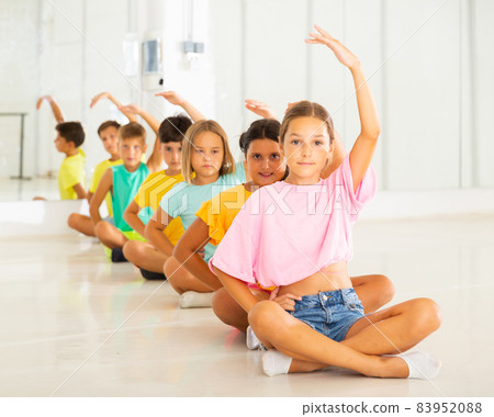 Preteens stretching sitting in row one by one on floor in choreography class Preteens stretching sitting in row one by one on floor in choreography class 83952088