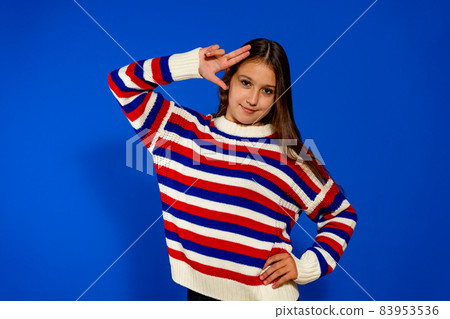 Portrait of little kid girl. Bronw hair child in striped sweater. Happy positive kid isolated on blue background with copy space. body language concept. Like gesture. Stylish school girl 83953536