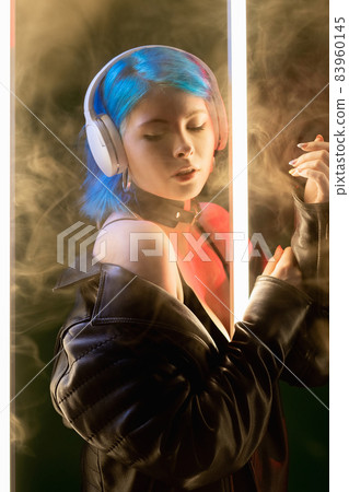 Music vibe. Song chill. Futuristic technology. Inspired gentle cyberpunk woman in headphones enjoying playlist in LED neon light on smoke dark background. Music vibe. Song chill. Futuristic technology. Inspired gentle cyberpunk woman in headphones enjoying playlist in LED neon light on smoke dark background. 83960145