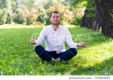 Young man meditates in lotus pose on green grass Young man meditates in lotus pose on green grass 83960691