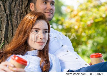 Young couple relaxing with coffee under tree Young couple relaxing with coffee under tree 83960693