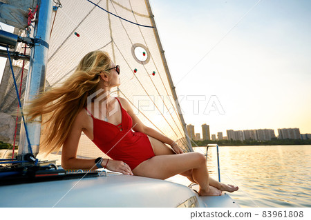 Young beautiful woman in fashion red swimsuit standing on yacht in open sea or ocean, sailing 83961808