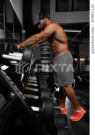Brutal handsome Caucasian bodybuilder working out training in the gym gaining weight pumping up muscles and poses fitness and bodybuilding concept 83962116