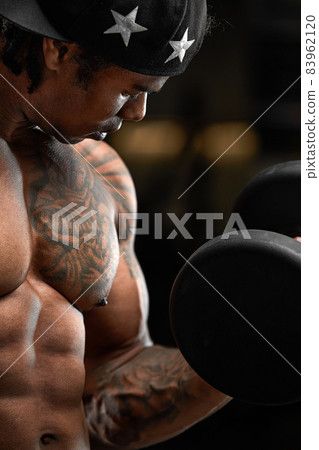 Strong and muscular dark skin man trains on modern equipment in gym. Portrait of muscular pumped up fitness trainer Strong and muscular dark skin man trains on modern equipment in gym. Portrait of muscular pumped up fitness trainer 83962120