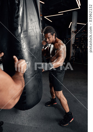 An African American guy trains in gym and fists his boxing bag fists. Concept of: gym, fitness, boxing, success, workout and power 83962132