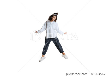 Studio shot of young woman in casual wear jumping, flying isolated on white background. Art, motion, action, flexibility, inspiration concept. 83963567