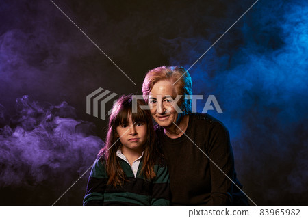 portrait of grandmother in the eighties and 5-year-old granddaughter with smoke and colored gels. great copy space portrait of grandmother in the eighties and 5-year-old granddaughter with smoke and colored gels. great copy space 83965982