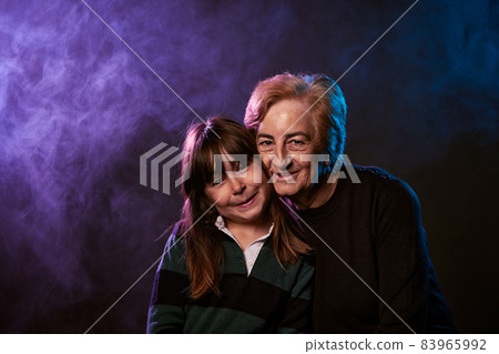 portrait of grandmother and granddaughter family smiling at camera with smoke and colored lights portrait of grandmother and granddaughter family smiling at camera with smoke and colored lights 83965992