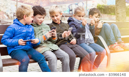 Children on bench with phones Children on bench with phones 83966148
