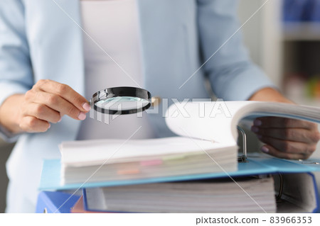 Businesswoman looking through magnifying glass tool on documents 83966353