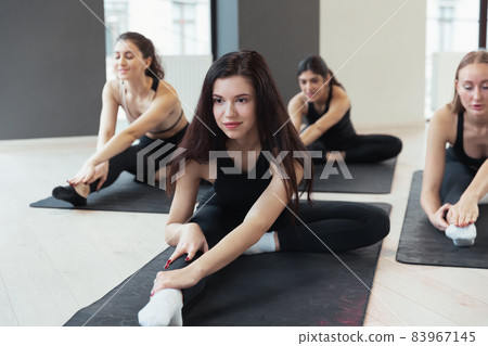 Close-up young sportive women in sportswear doing yoga exercises on sports mats at yoga meditation center. Concept of healthy lifestyle, wellbeing Close-up young sportive women in sportswear doing yoga exercises on sports mats at yoga meditation center. Concept of healthy lifestyle, wellbeing 83967145