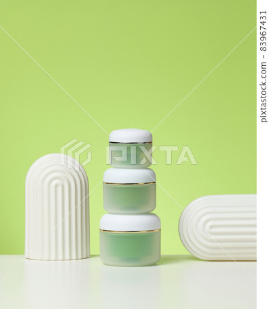 green jar for cosmetics on a white table. Packaging for cream, gel, serum, advertising and product promotion green jar for cosmetics on a white table. Packaging for cream, gel, serum, advertising and product promotion 83967431