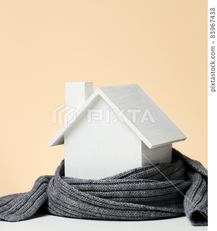 A white wooden miniature house wrapped in a gray knitted scarf. Building insulation concept, loans for repairs A white wooden miniature house wrapped in a gray knitted scarf. Building insulation concept, loans for repairs 83967438