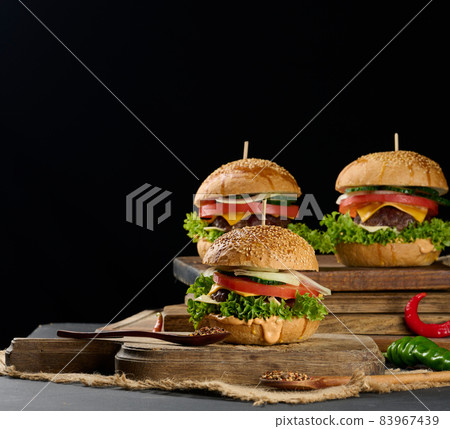 cheeseburger with grilled beef patty, cheddar cheese, tomato and lettuce on a wooden board, black background cheeseburger with grilled beef patty, cheddar cheese, tomato and lettuce on a wooden board, black background 83967439