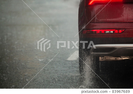 Rain water splash flow from wheels of red car moving fast in daylight city with selective focus. Rain water splash flow from wheels of red car moving fast in daylight city with selective focus. 83967689