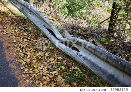 Dirty guardrail in the mountains, which seems to be dented by a fallen tree 83968159