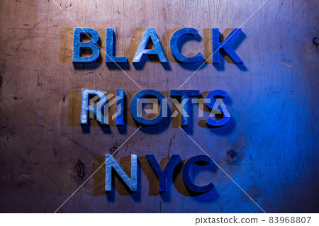 The words black riots NYC laid with metal letters on flat plywood surface under white and blue police lights. Concept. The words black riots NYC laid with metal letters on flat plywood surface under white and blue police lights. Concept. 83968807