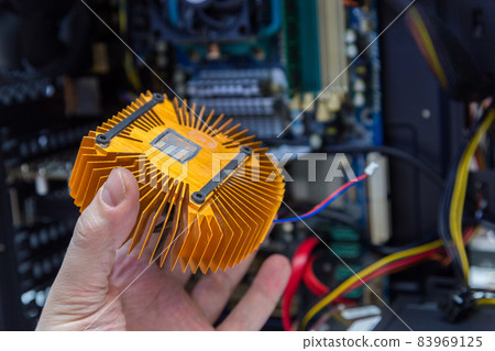 caucasian hand holding orange plated computer heatsink and pc internals in blurry background caucasian hand holding orange plated computer heatsink and pc internals in blurry background 83969125