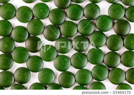 many green organic spirulina tablets laid ramdomly in one layer on flat white surface 83969170