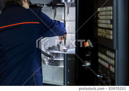 The operator of 5-axis cnc milling machine changes the workpiece in a collet chuck. Selective focus on background. 83970201