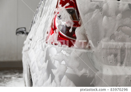 a car covered by soap foam while washing indoors - close-up wiew from back with selective focus 83970296