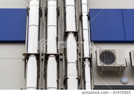 Chrome ventilation pipes on the outside wall of the white and blue Industrial building 83970885