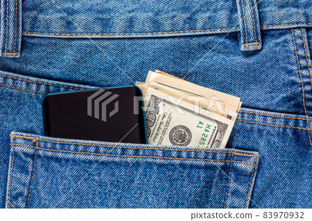 US dollar banknotes and smartphone in the left rear pocket of blue jeans. 83970932
