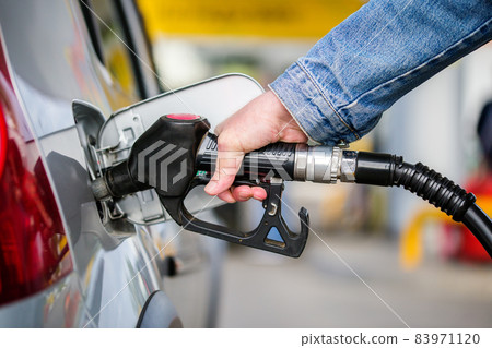 a person in jeans jacket refueling gray metallic car on gas station at daylight - close-up in horizontal composition 83971120
